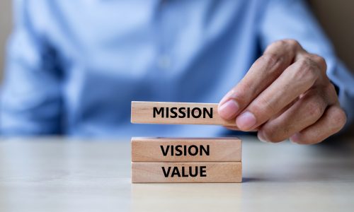 Businessman hand holding wooden building blocks with MISSION, VISION, CORE VALUE Concepts
